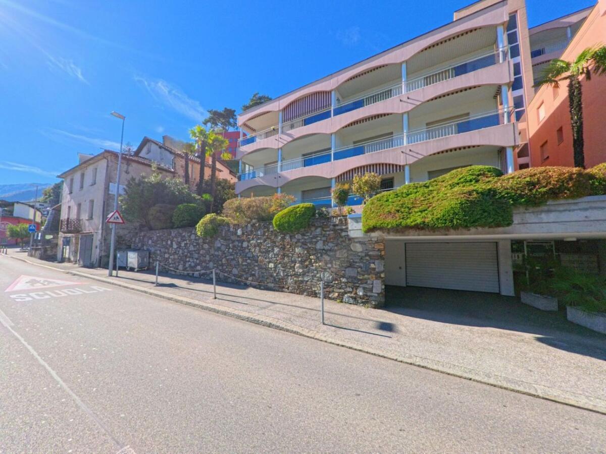 In Brissago (6614, Kanton Tessin) stehen moderne Wohnhäuser mit Balkonen neben älteren Gebäuden an einer sonnigen Strasse mit Palmen.