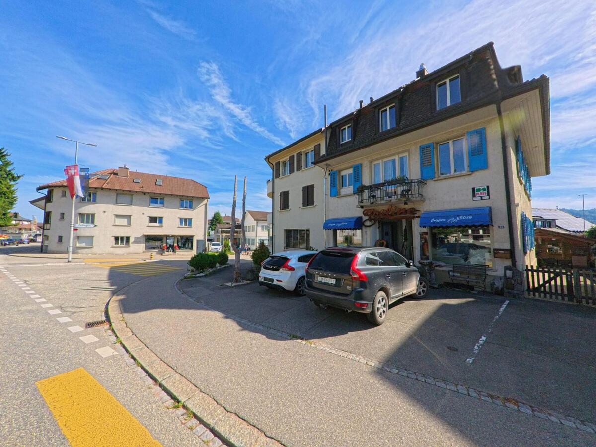 Im Zentrum von Brittnau (4805, Kanton Aargau) befindet sich ein Geschaeftshaus mit blauen Fensterlaeden und einer Confiserie an einer verkehrsreichen Kreuzung.