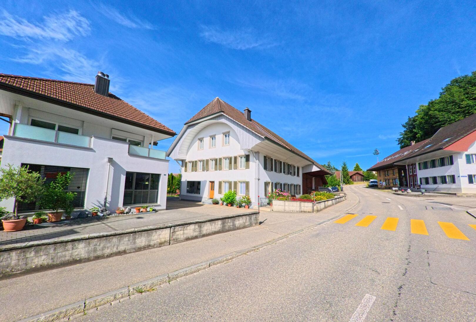 Im Ortskern von Brittnau (4805, Kanton Aargau) saeumen gepflegte Wohnhaeuser mit Blumenbeeten eine leicht ansteigende Strasse mit Zebrastreifen.