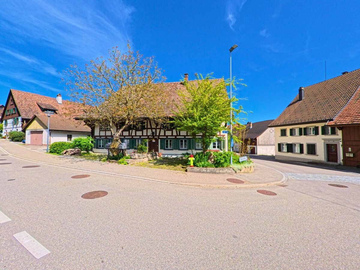 Im historischen Zentrum von [ORT] 8311 im [KANTON] Zürich stehen mehrere gut erhaltene Fachwerkhäuser an einer verkehrsberuhigten Kreuzung mit Bauminsel.