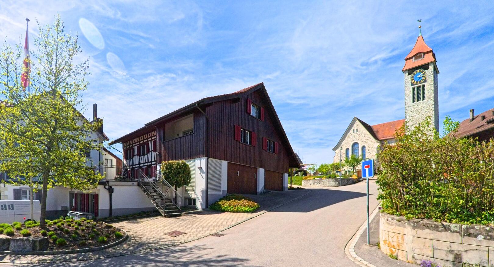 Im Brütten 8311 im Zürich führt eine ruhige Strasse an traditionellen Wohnhäusern und der markanten Kirche mit Uhrturm vorbei.