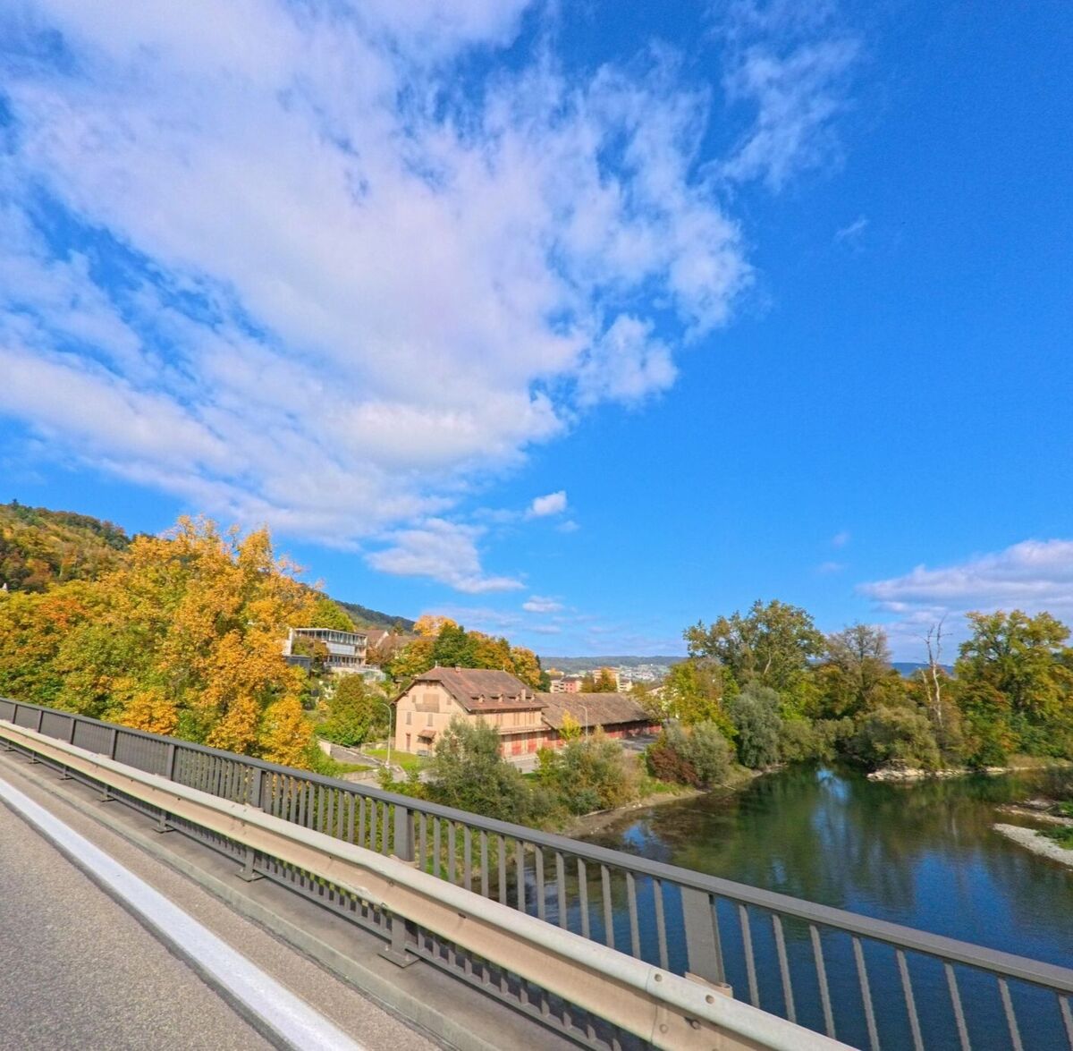 Von einer Brücke in Brugg (5200, Kanton Aargau) bietet sich ein Blick auf die Aare mit ihren Uferbäumen und den herbstlich gefärbten Hängen im Hintergrund.