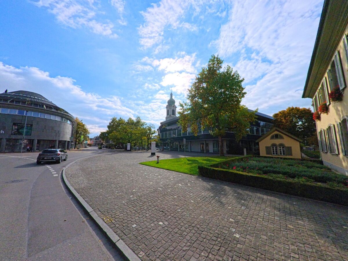 In der Altstadt von Brugg (5200, Kanton Aargau) öffnet sich ein Platz mit Kopfsteinpflaster, modernen Gebäuden und der Kirchturmspitze im Hintergrund.