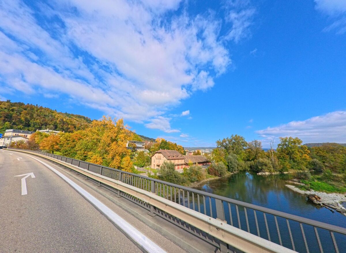 Ueber einer Flusslandschaft mit herbstlichen Baumen fuehrt in Brugg (5200, Kanton Aargau) eine breite Bruecke, von der aus sich der Blick auf die Uferzone von [ORT] eroefnet.
