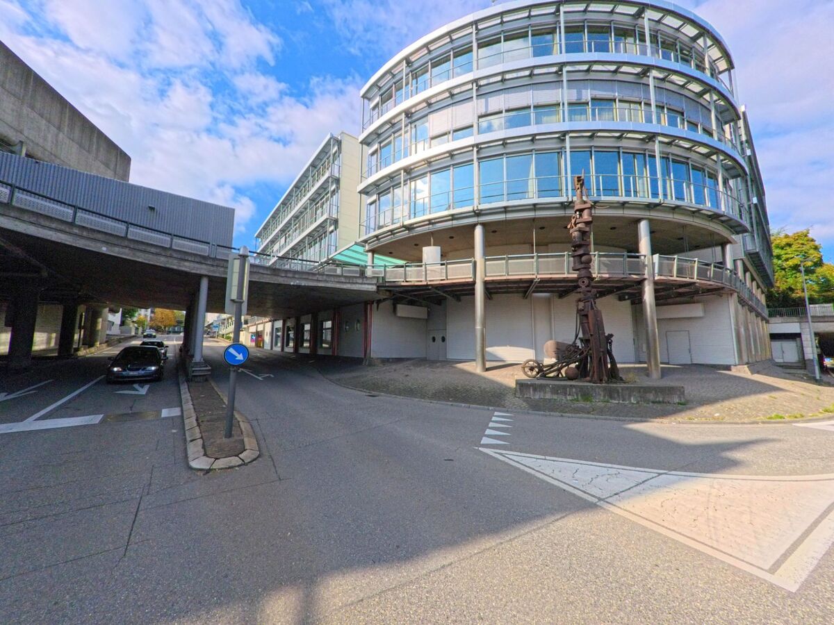 Ein modernes Gebäude mit Glasfassade und einer Metallskulptur steht in Brugg (5200, Kanton Aargau) an einer Strassenkreuzung unterhalb einer Hochstrasse.