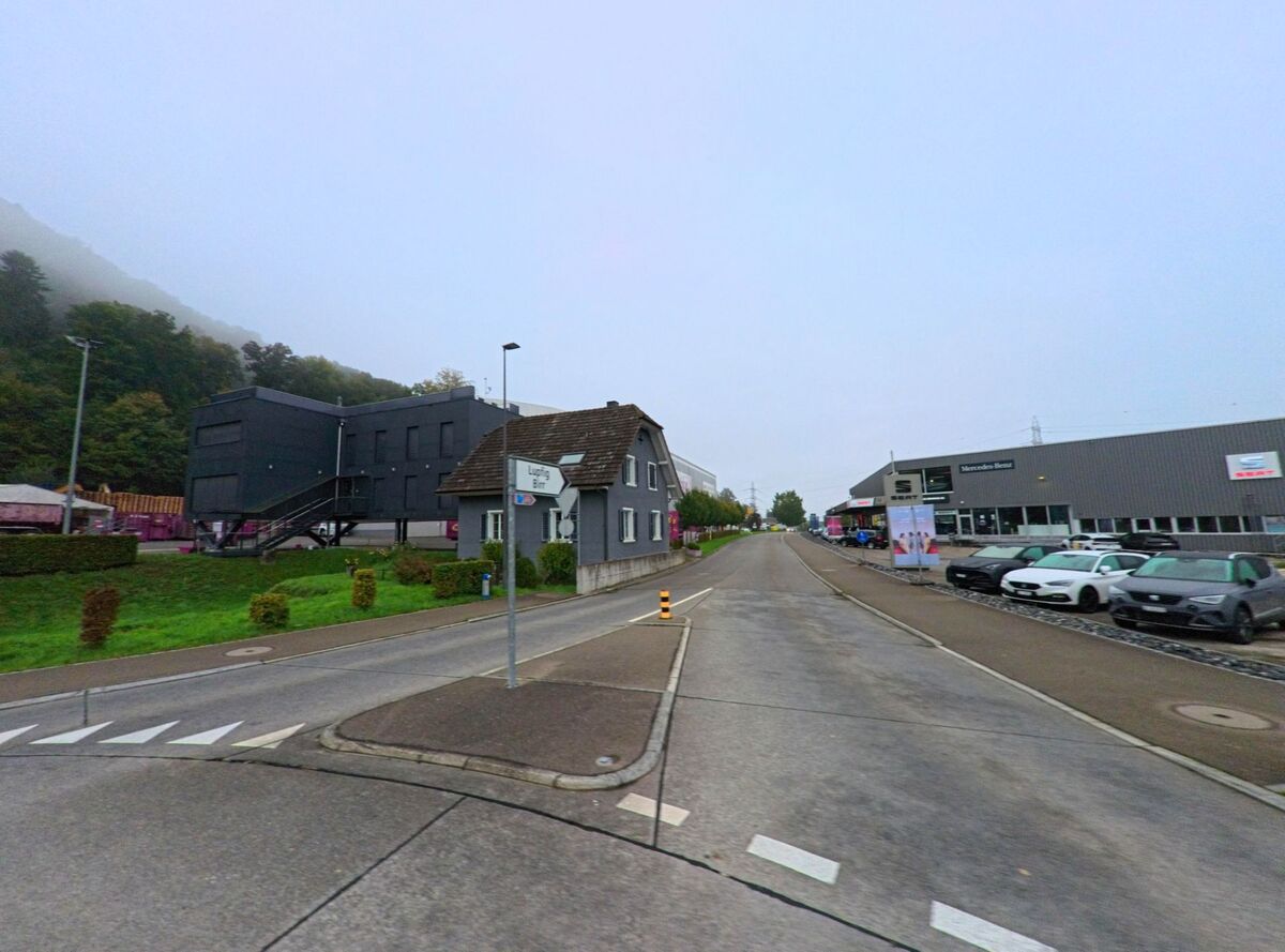 In Brunegg (5505, Kanton Aargau) verläuft eine Strasse mit Autohäusern und Gewerbebauten, eingerahmt von Hügeln im morgendlichen Nebel.