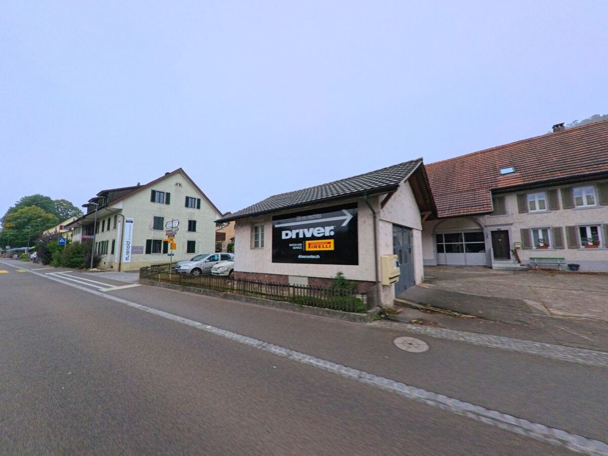 Entlang der Hauptstrasse in Brunegg (5505, Kanton Aargau) stehen ältere Wohn- und Gewerbegebäude mit traditionellen Fassaden und dunklen Fensterläden.