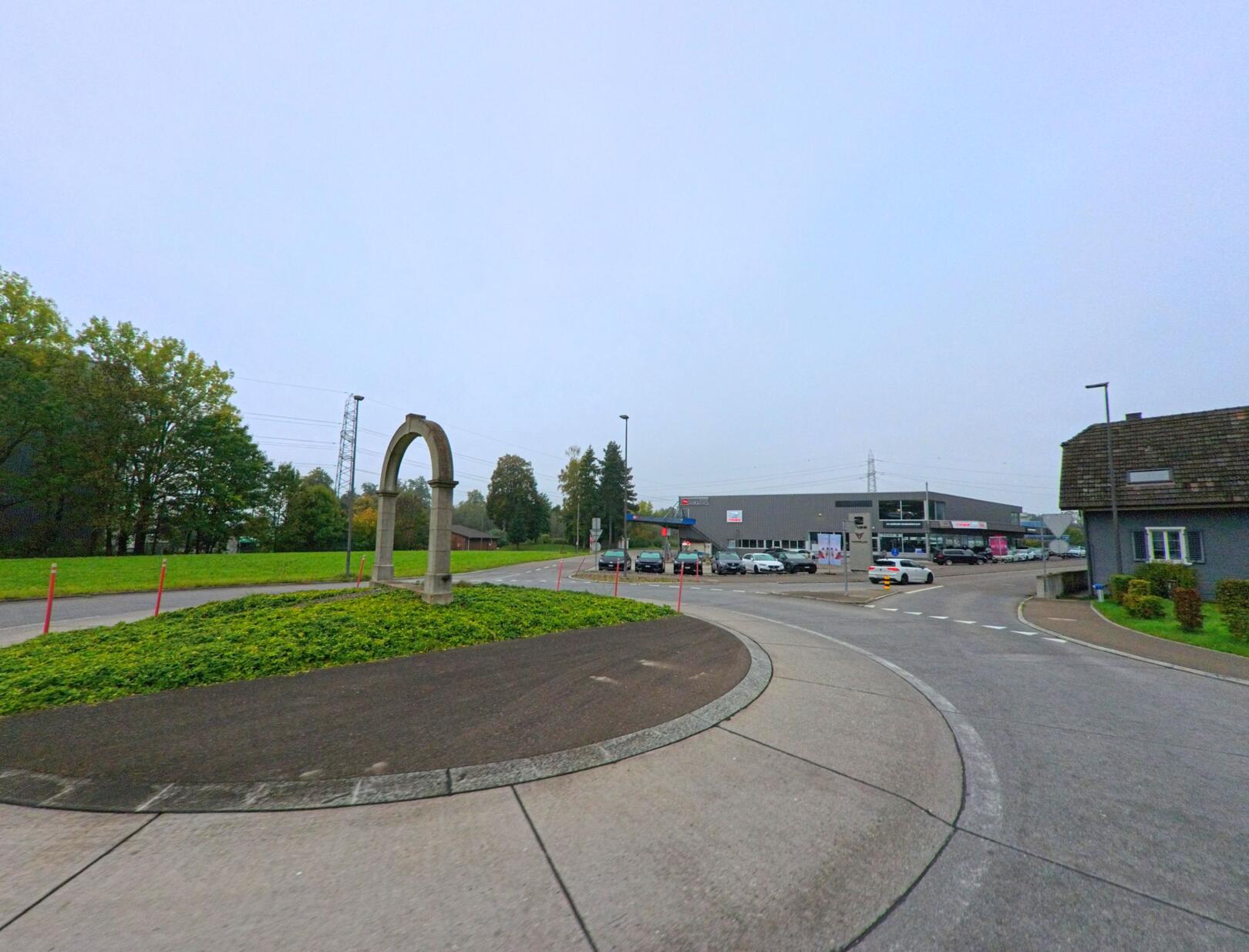 In Brunegg (5505, Kanton Aargau) steht in einem Kreisverkehr ein steinerner Torbogen, umgeben von Grünflächen und angrenzenden Gewerbebauten.