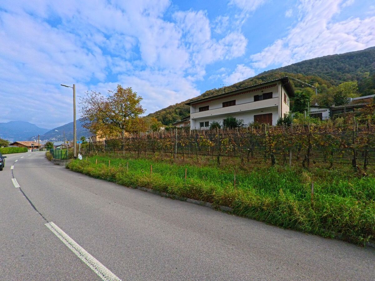 An der leicht kurvigen Strasse in Brusino Arsizio (6827, Kanton Tessin) steht ein Haus oberhalb eines kleinen Weinbergs mit Blick auf die Berge des Luganese.