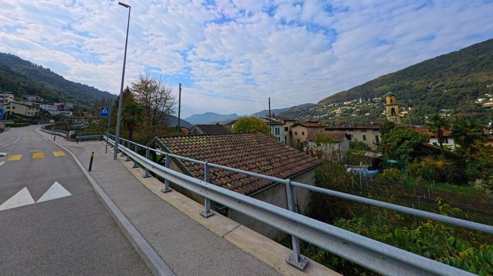 Von der leicht ansteigenden Strasse in Brusino Arsizio (6827, Kanton Tessin) bietet sich ein weiter Blick über die Dächer des Dorfes bis zu den umliegenden Hügeln.