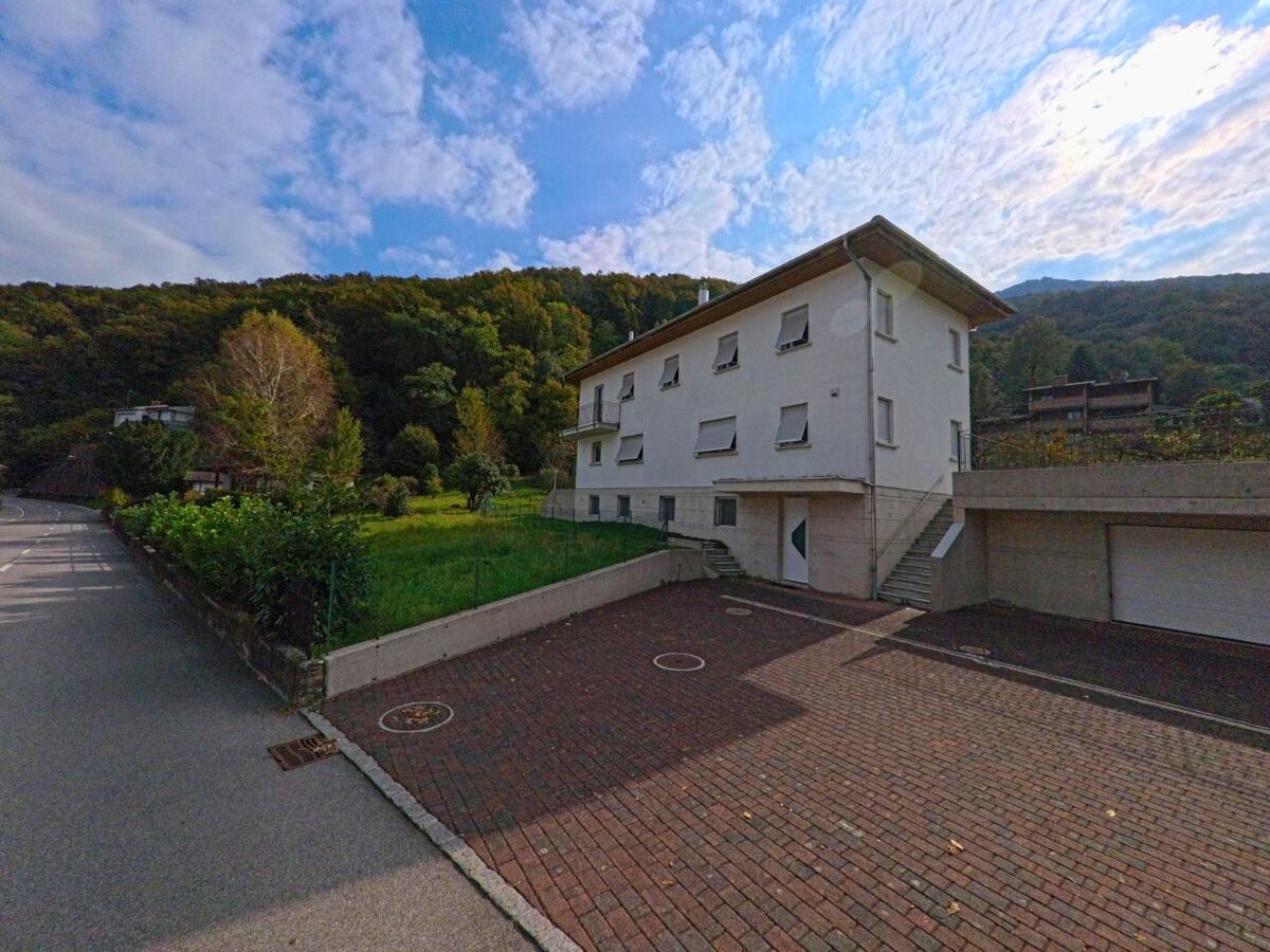 Ein helles Wohnhaus mit gepflasterter Einfahrt steht am Waldrand von Brusino Arsizio (6827, Kanton Tessin) in ruhiger Lage am Hang.