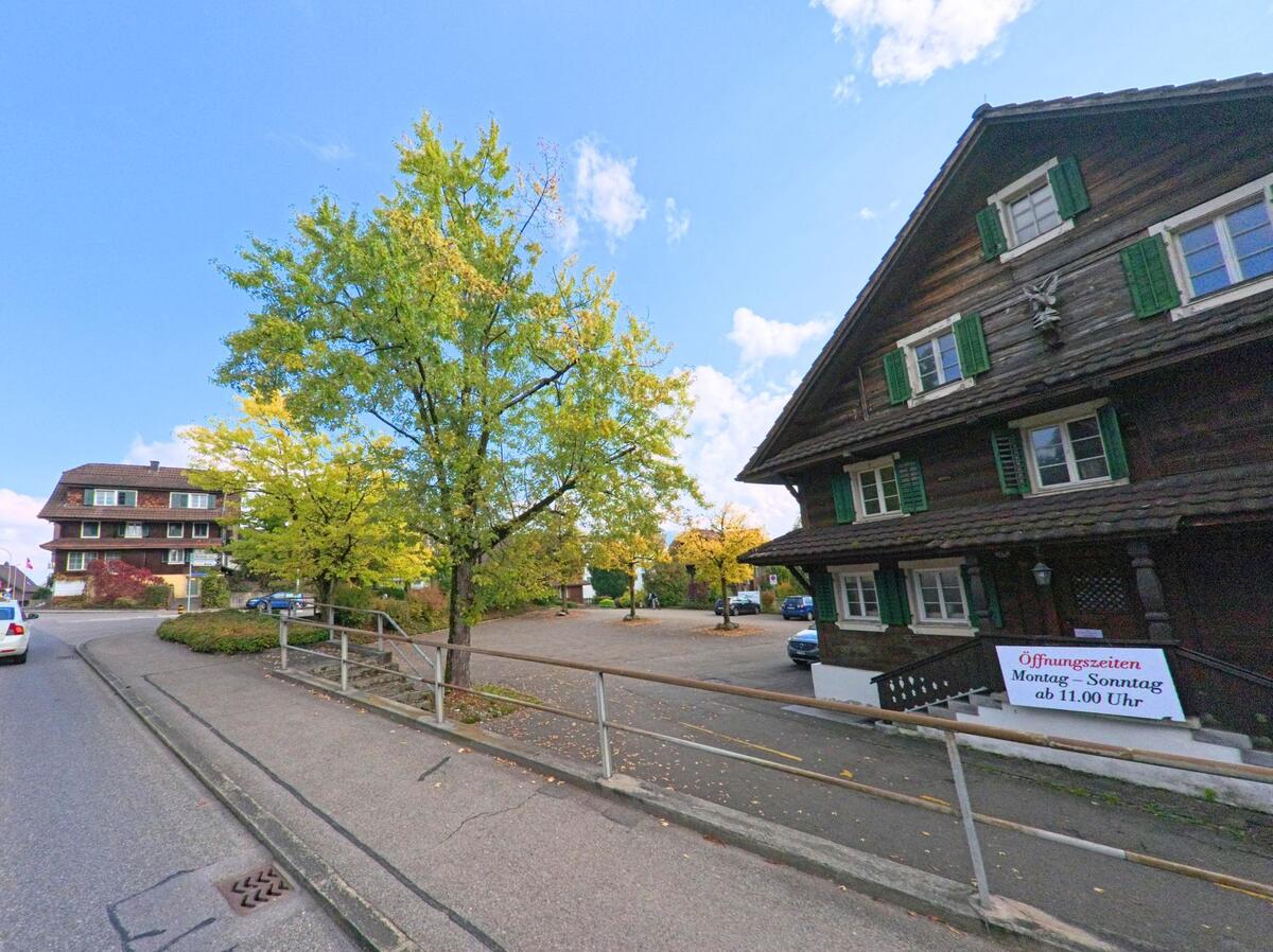 In Buchrain (6033, Kanton Luzern) stehen traditionelle Holzhäuser mit grünen Fensterläden entlang einer ruhigen Strasse.
