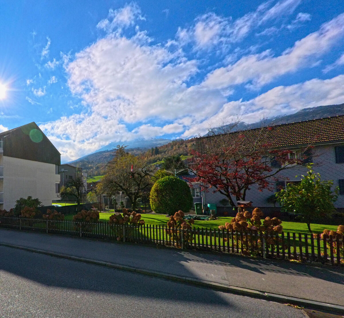 Ein gepflegter Garten mit Herbstfarben liegt vor Wohnhaeusern in Buchs (9470, Kanton St. Gallen) bei Sonnenschein.