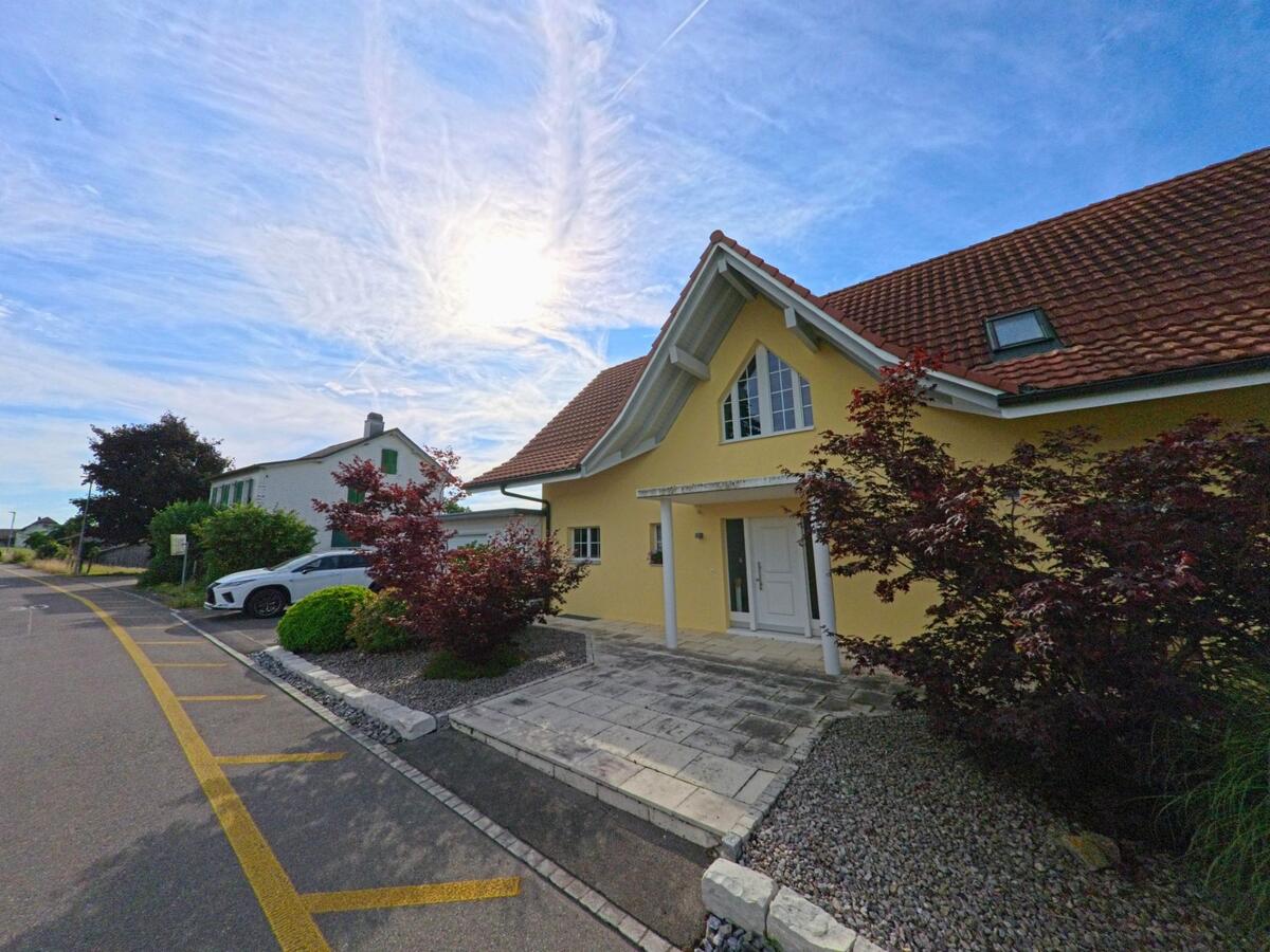 In Bühl (3274, Kanton Bern) steht ein gelbes Einfamilienhaus mit gepflegtem Vorgarten und rotem Ziegeldach an einer ruhigen Quartierstrasse.