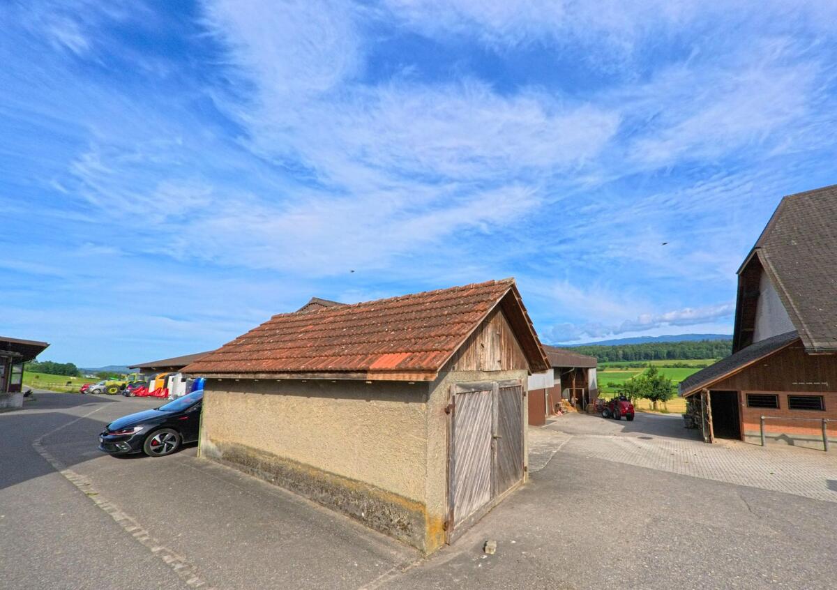 Am Rande von Bühl (3274, Kanton Bern) stehen einfache landwirtschaftliche Nebengebäude mit Blick auf Felder und Wälder im Hintergrund.