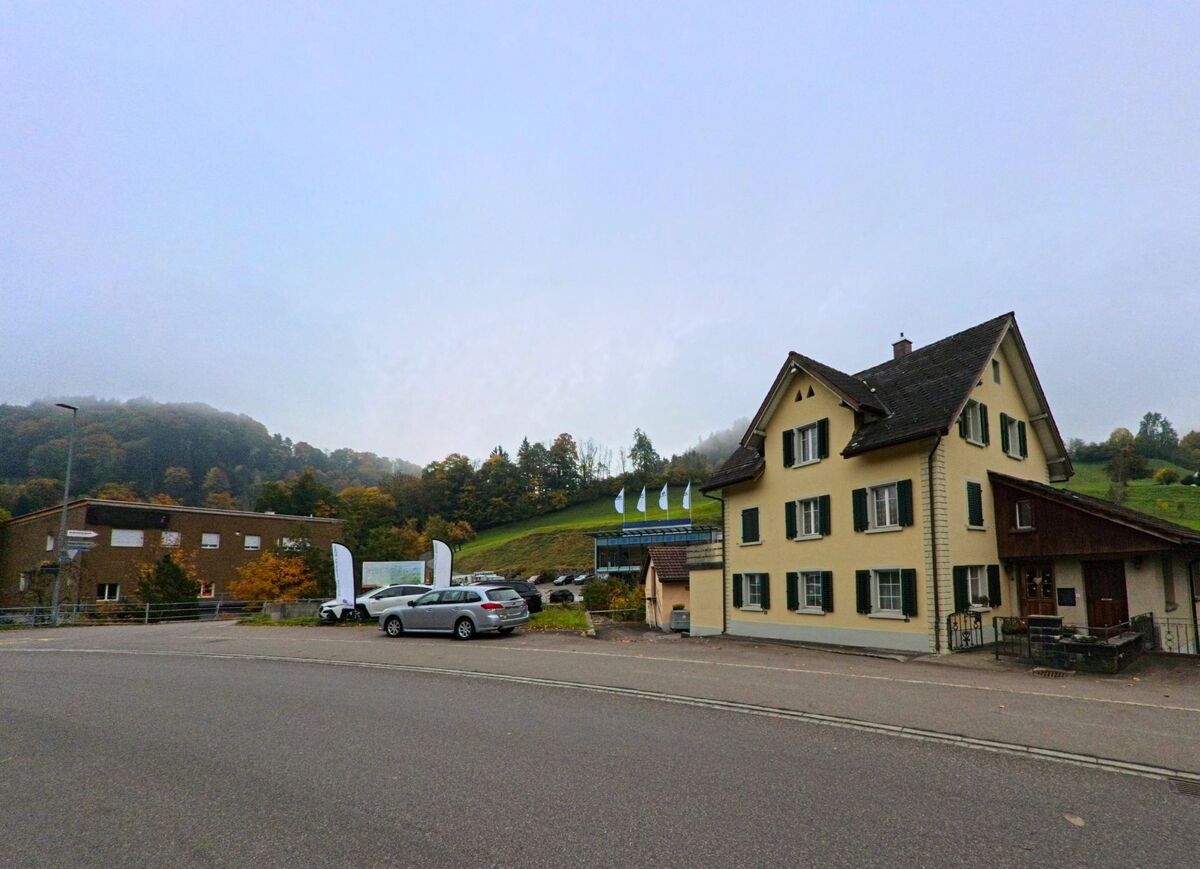 Vor einem Wohnhaus öffnet sich ein kleiner Platz mit parkierenden Fahrzeugen in Bühler (9055, Kanton Appenzell Ausserrhoden).