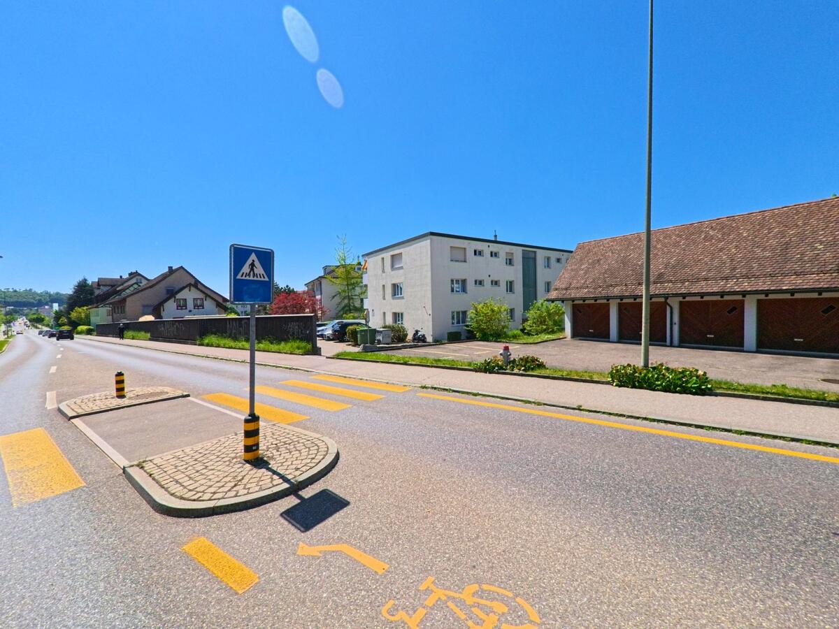 In Bülach im PLZ-Gebiet 8180 im Kanton Zürich befindet sich ein Fussgängerstreifen mit Verkehrsinsel vor einer Wohnsiedlung und Garagenreihe.