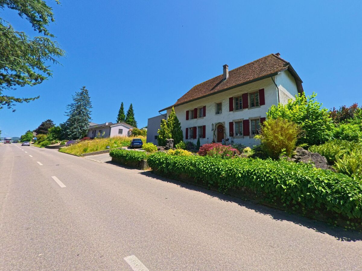 An einer leicht ansteigenden Strasse in Büren an der Aare (3294, Kanton Bern) liegt ein gepflegtes Landhaus mit roten Fensterlaeden und vorgelagertem Garten.