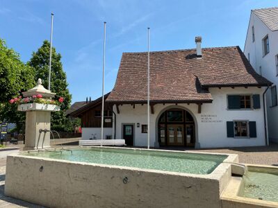 Brunnenanlage mit Wasserbecken vor dem historischen Buergerhaus in Pratteln (4133, Kanton Baselland), sonniger Dorfplatz mit traditioneller Architektur.