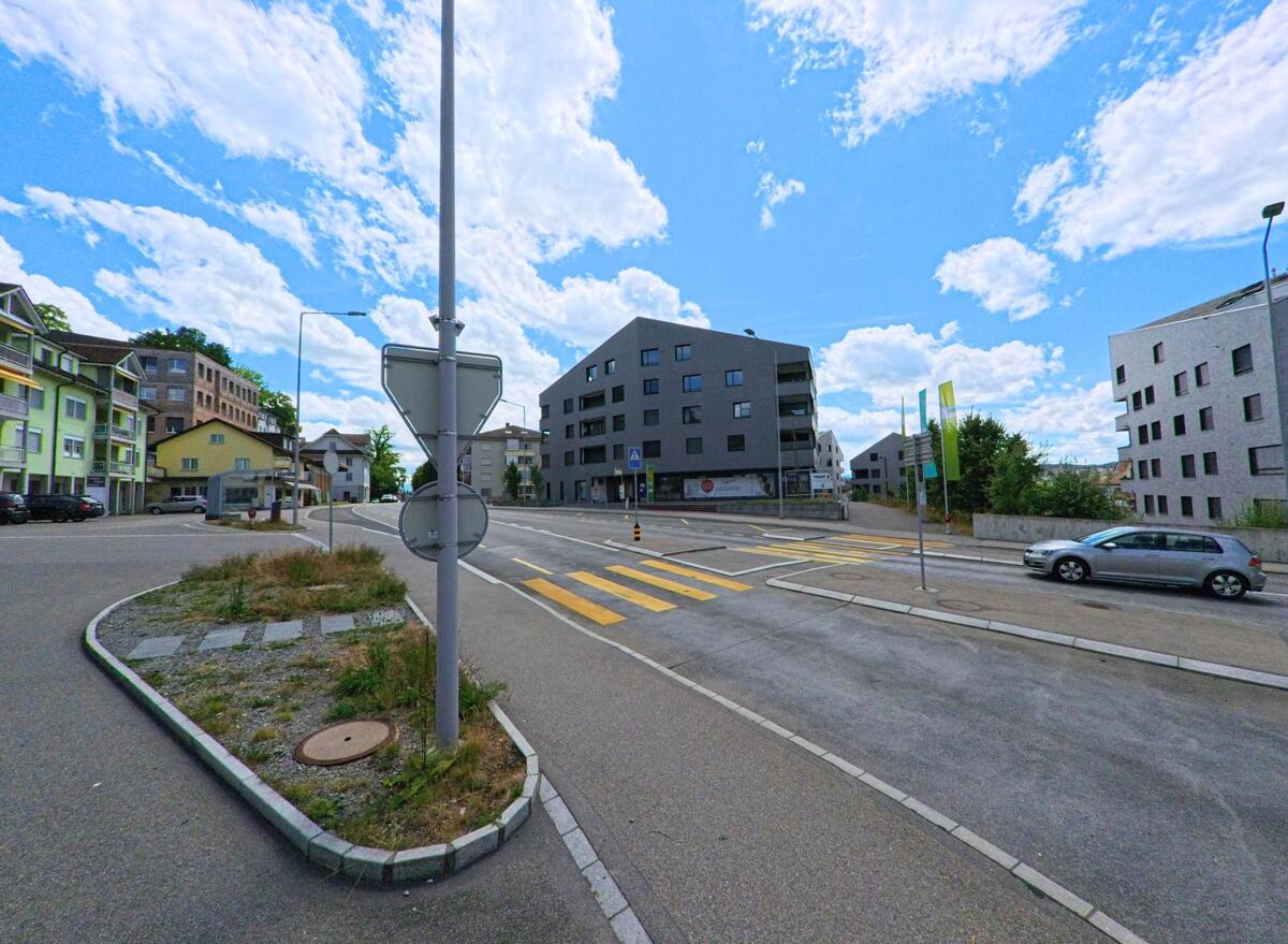  In Bueron (6233, Kanton Luzern) treffen an einer vielbefahrenen Kreuzung moderne Wohnbauten auf aeltere Mehrfamilienhaeuser, mit markierten Fussgaengerstreifen und Verkehrsinsel.