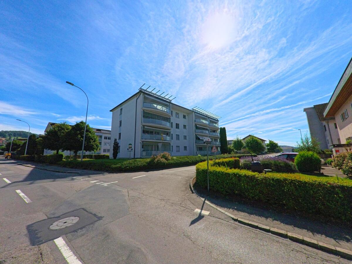 In einem Wohnquartier von Bueron (6233, Kanton Luzern) stehen moderne Mehrfamilienhaeuser mit verglasten Balkonen entlang begruenter Strassen und gepflegter Gartenanlagen.
