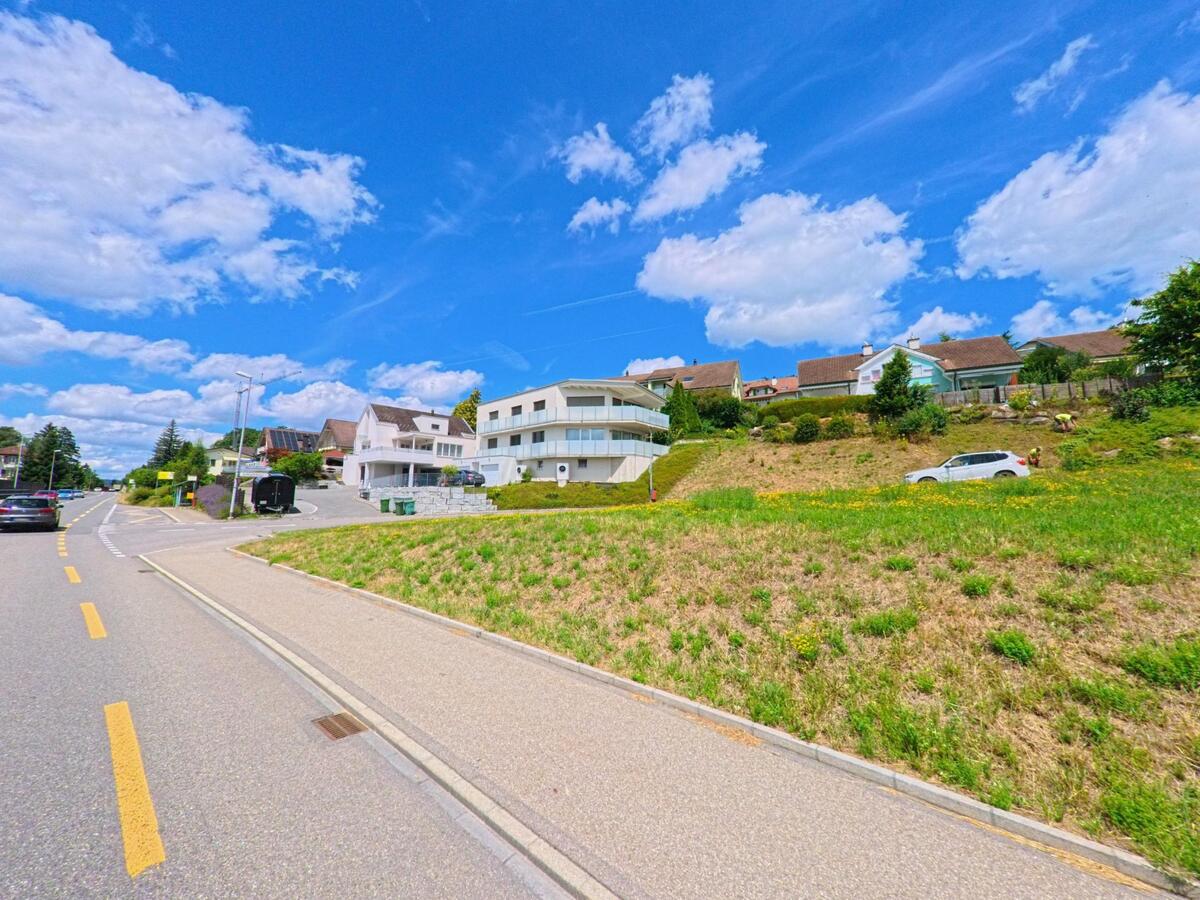 In Bueron (6233, Kanton Luzern) verlaeuft eine leicht ansteigende Strasse an modernen Einfamilienhaeusern vorbei, flankiert von gruener Hanglage und einem Gehweg.