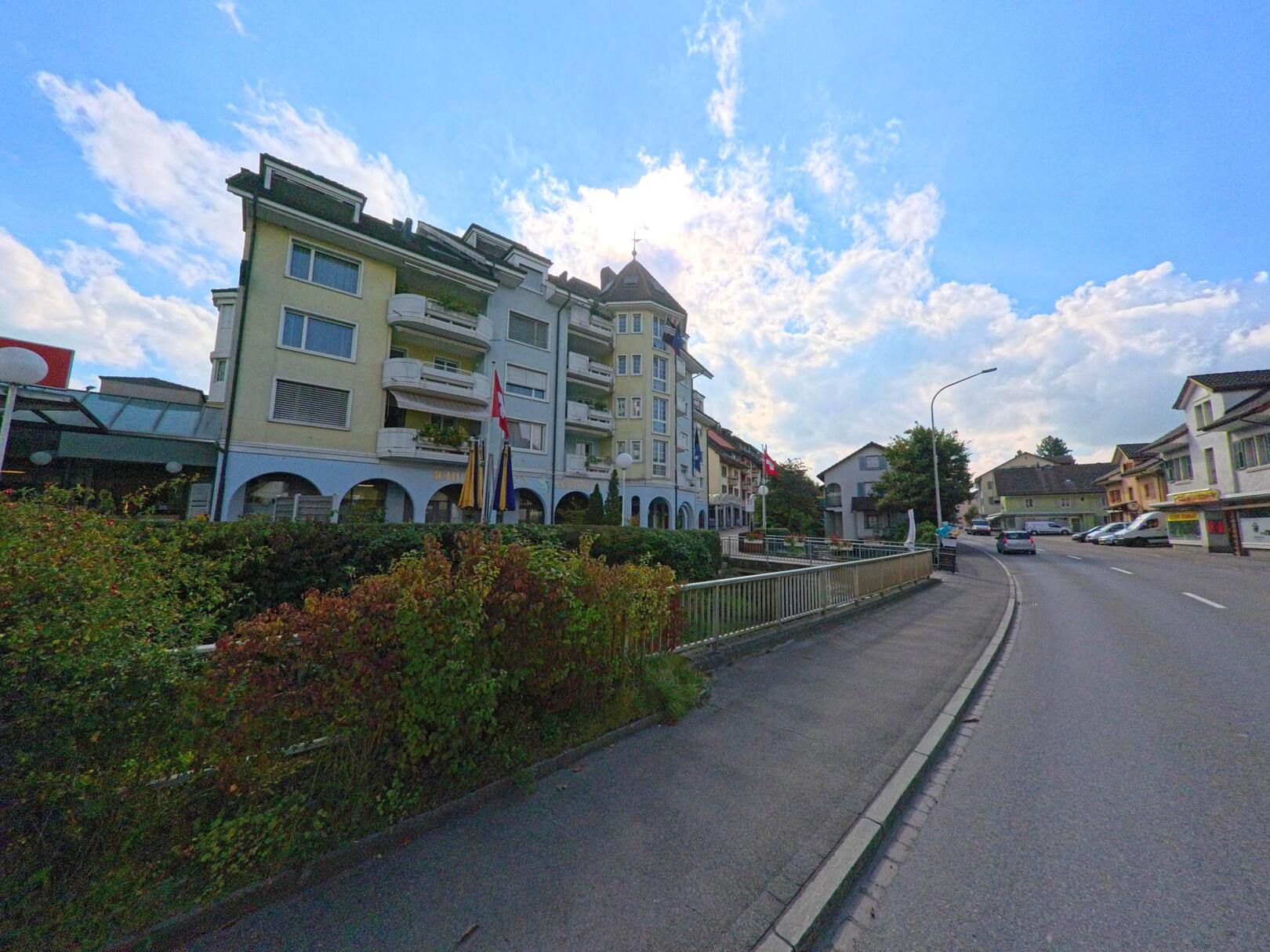 Mehrstöckige Wohn- und Geschäftshäuser mit Arkaden prägen das Strassenbild im Zentrum von Burg (5737, Kanton Aargau) an einem sonnigen Nachmittag.