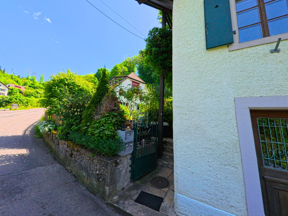 In Burg im Leimental (4117, Kanton Baselland) führt eine leicht ansteigende Strasse an liebevoll bepflanzten Vorgärten und traditionellen Wohnhäusern vorbei.