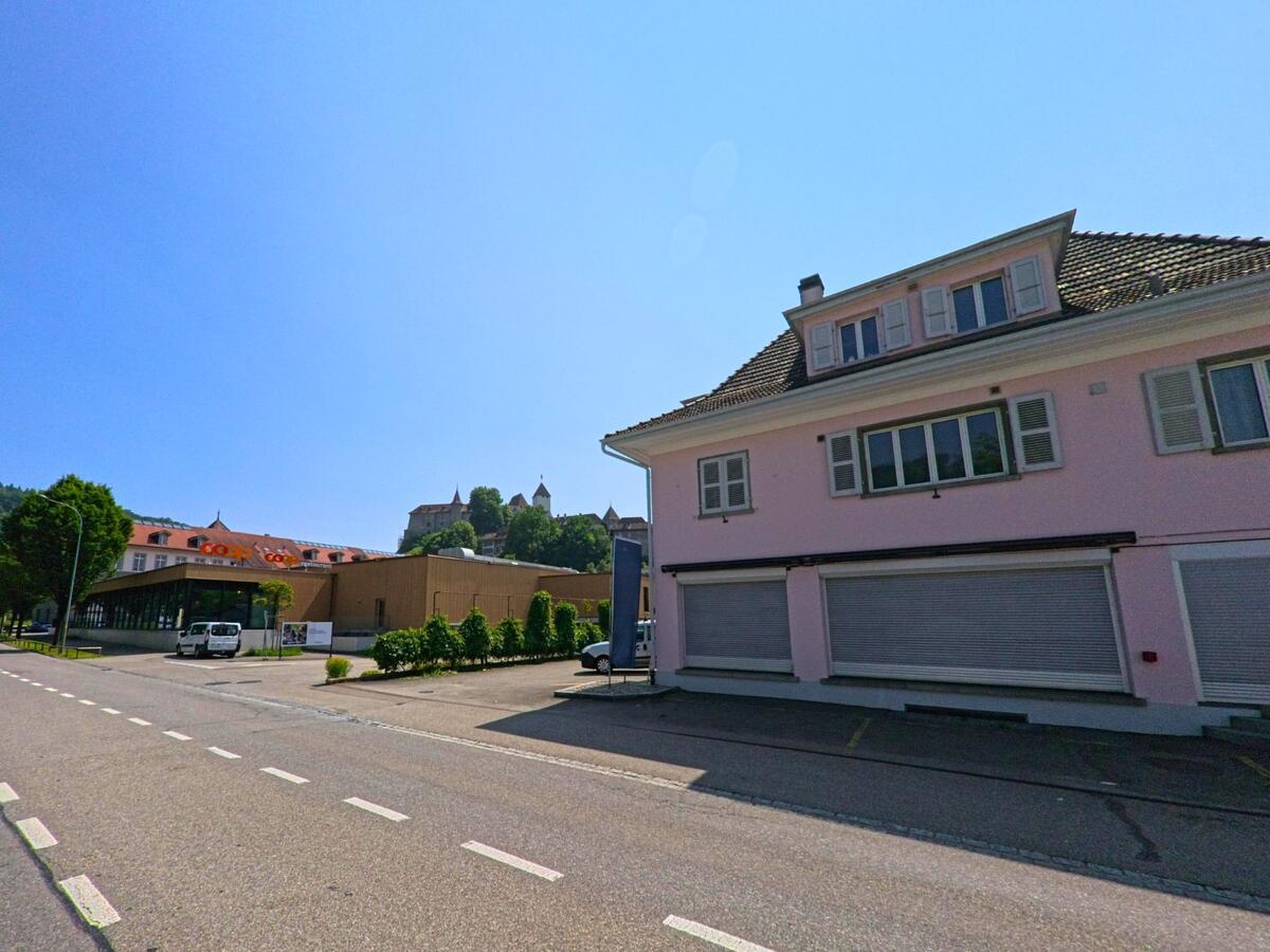  In Burgdorf (3400, Kanton Bern) steht ein rosa Wohn- und Geschäftshaus gegenüber einem Coop-Gebäude mit dem Schloss im Hintergrund.