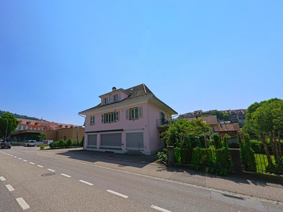 In Burgdorf (3400, Kanton Bern) steht ein rosa Wohnhaus mit geschlossenen Fensterläden an einer ruhigen Strasse, im Hintergrund ist ein Coop-Gebäude erkennbar.