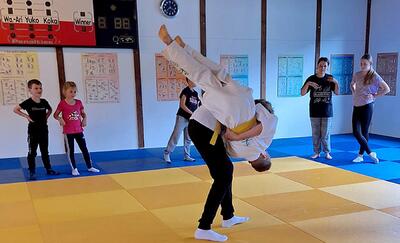 In Frick (5070, Kanton Aargau) zeigt ein junger Judoka mit gelbem Guertel auf der Matte eine Wurftechnik, waehrend andere Kinder aufmerksam zuschauen.