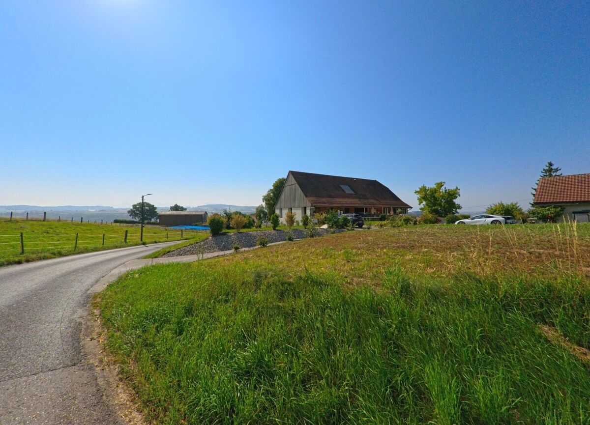 Eine schmale Landstrasse fuehrt durch Felder am Ortsrand von Bussy-sur-Moudon (1514, Kanton Waadt) vorbei an einem grossen Wohnhaus.