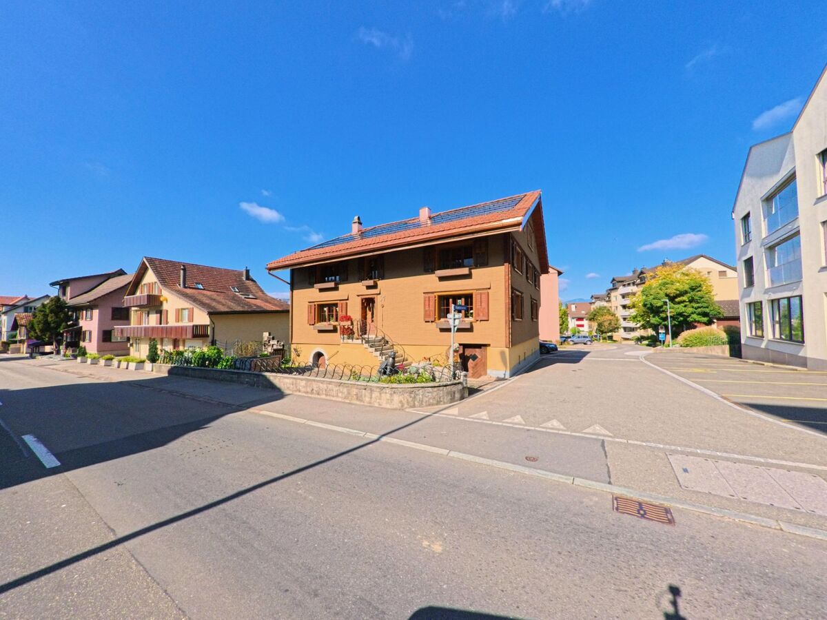 An einer ruhigen Kreuzung in Buttikon (8862, Kanton Aargau) steht ein freistehendes Wohnhaus mit Satteldach, Fensterläden und kleinem Vorgarten, umgeben von weiteren Wohngebäuden.