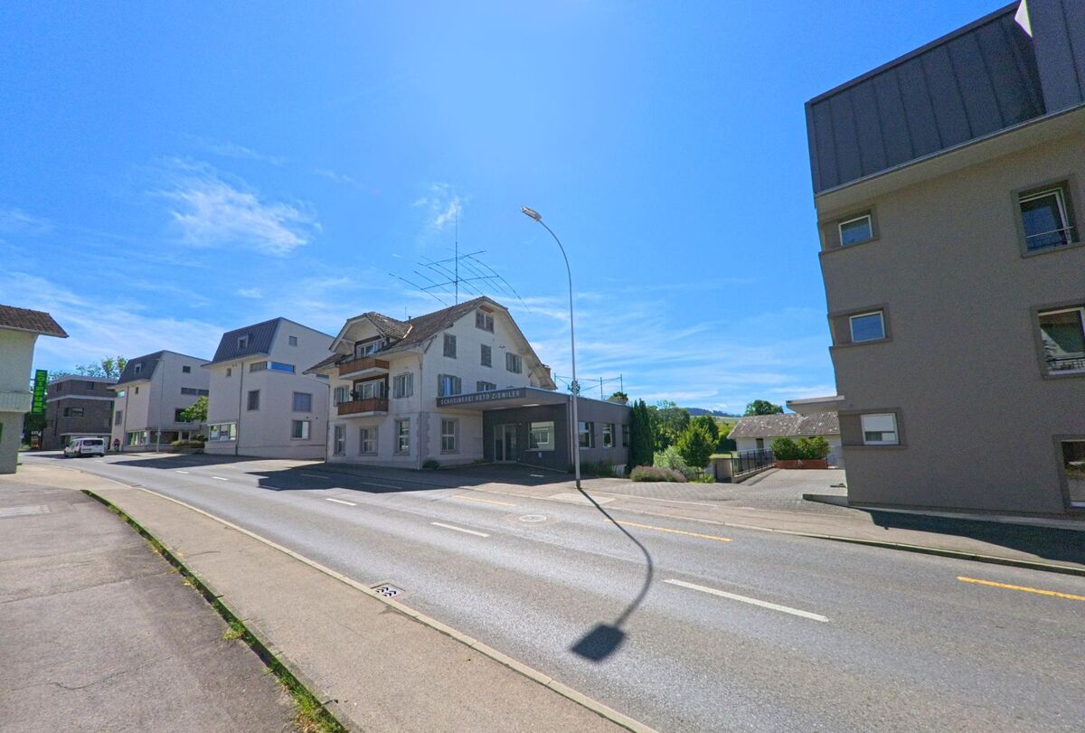 In Buttisholz (6018, Kanton Luzern) steht ein Gebaeude mit der Aufschrift „Schreinerei Reto Ziswiler“ an einer Hauptstrasse, umgeben von weiteren Wohn- und Gewerbebauten bei strahlendem Sonnenschein.