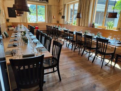 In Moerschwil (9402, Kanton St. Gallen) ist der helle Gastraum des Restaurants Buurebeiz mit langen Holztischen, schwarzen Stuehlen und dekorierten Gedecken vorbereitet.
