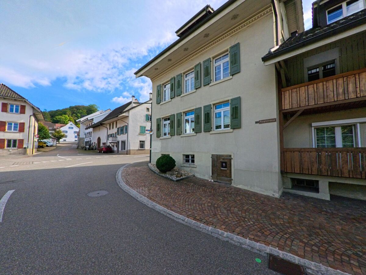 Im Zentrum von Buus (4463, Kanton Basel-Landschaft) saeumen traditionelle Wohnhaeuser mit Fensterlaeden und Holzveranden die leicht gekruemmte Hauptstrasse.