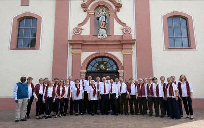 Eine grosse Gruppe von Saengerinnen und Saengern steht vor einer Kirche in Gurmels (3212, Kanton Freiburg) und zeigt Chorgemeinschaft.