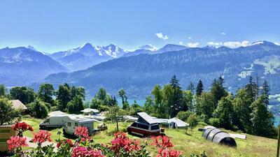 Der Camping Wang in Beatenberg (3803, Kanton Bern) liegt oberhalb des Thunersees mit Blick auf verschneite Alpen und blühende Sommerwiesen.