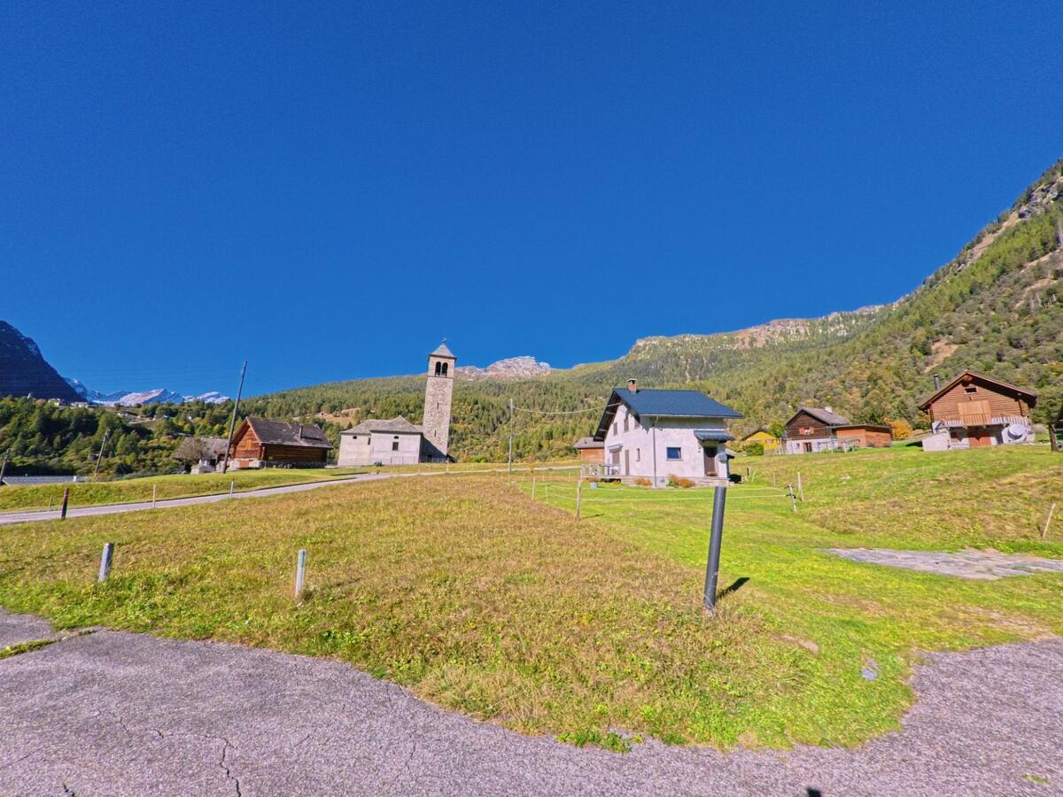 In Campo (6684, Kanton Tessin) liegt eine kleine Häusergruppe mit einer alten Kirche und ihrem hohen Glockenturm inmitten einer sonnigen Bergwiese.