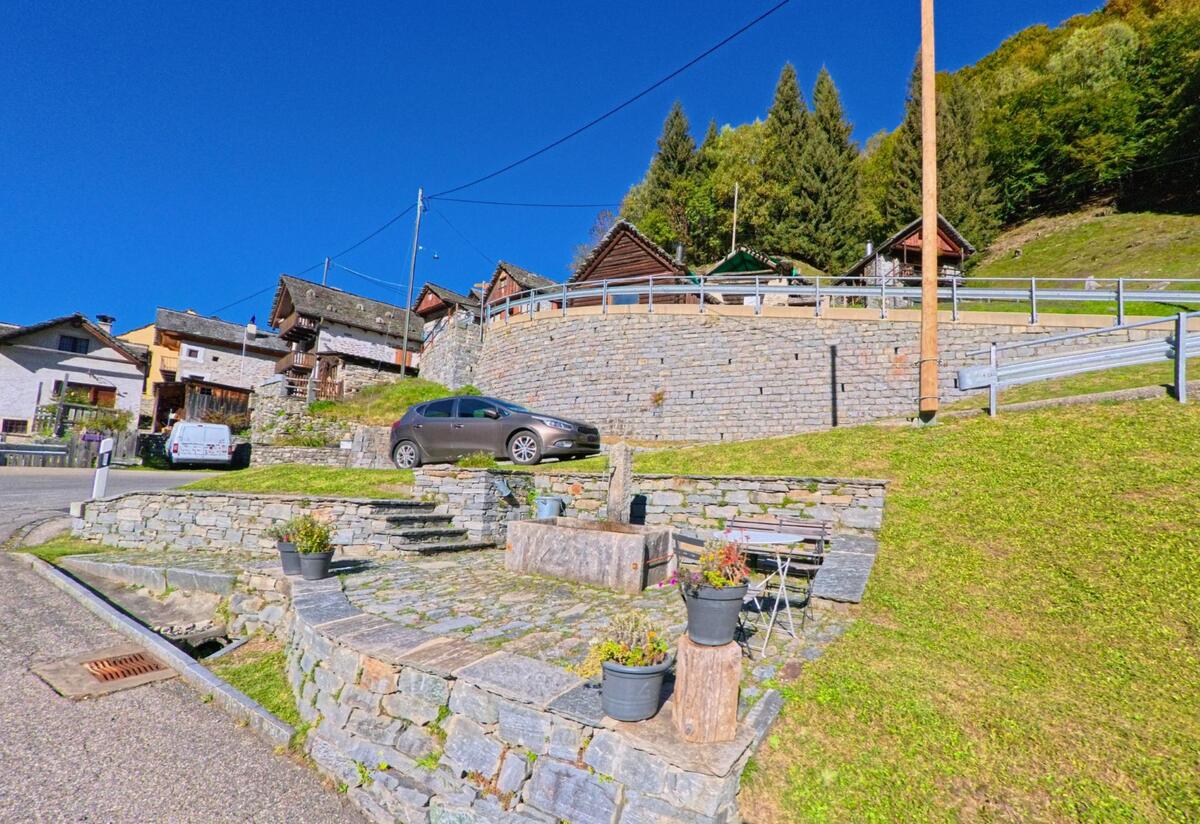 Terrassen aus Stein mit Sitzbank und Pflanztöpfen liegen in Campo (6684, Kanton Tessin) unterhalb traditioneller Häuser, die an einem sonnigen Hang erbaut sind.