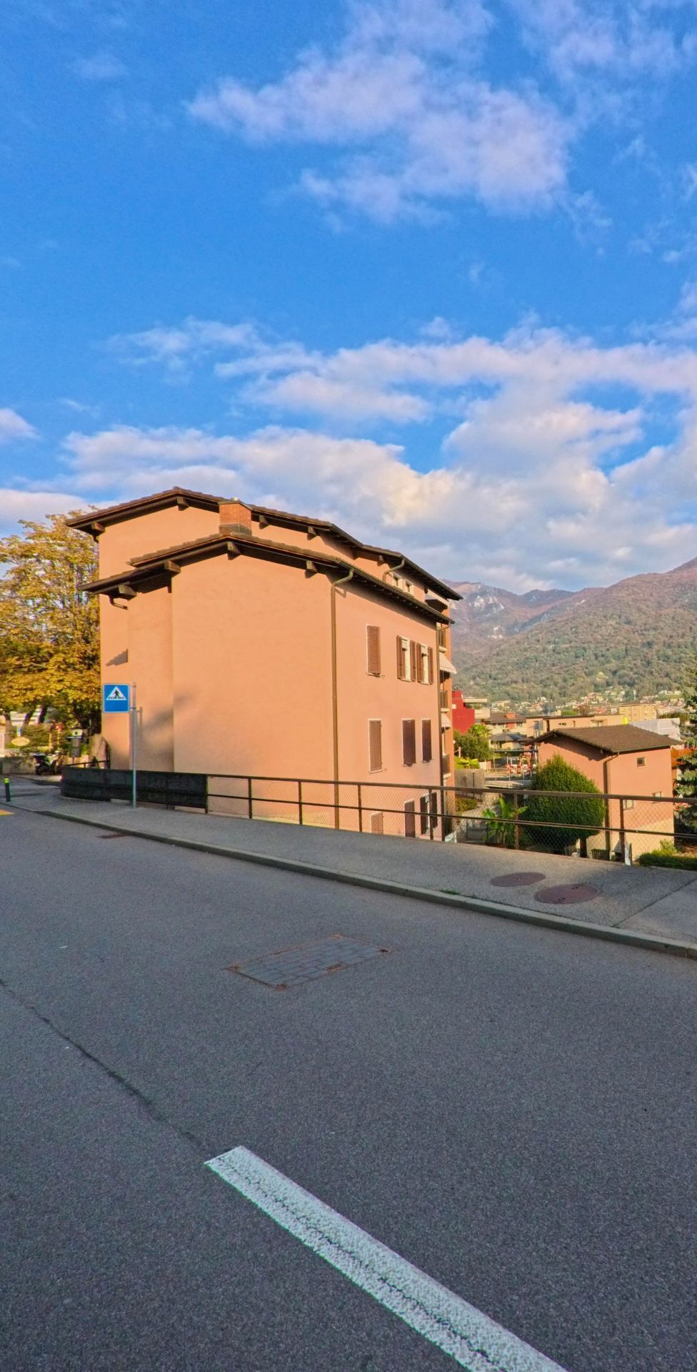 Ein Wohnhaus mit Strassenrand und Fussgaengerueberweg steht in Canobbio (6952, Kanton Tessin) mit freiem Blick auf das Tal und die umliegenden Berge.