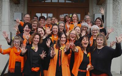Die Sängerinnen von canTanten posieren in schwarz-oranger Kleidung gut gelaunt für ein gemeinsames Gruppenfoto in Unterentfelden (5035, Kanton Aargau).