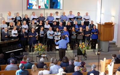 In einer Kirche in Muri-Gümligen (3073, Kanton Bern) steht ein Chor mehrreihig vor dem Altar und singt unter der Leitung eines Dirigenten vor Publikum.
