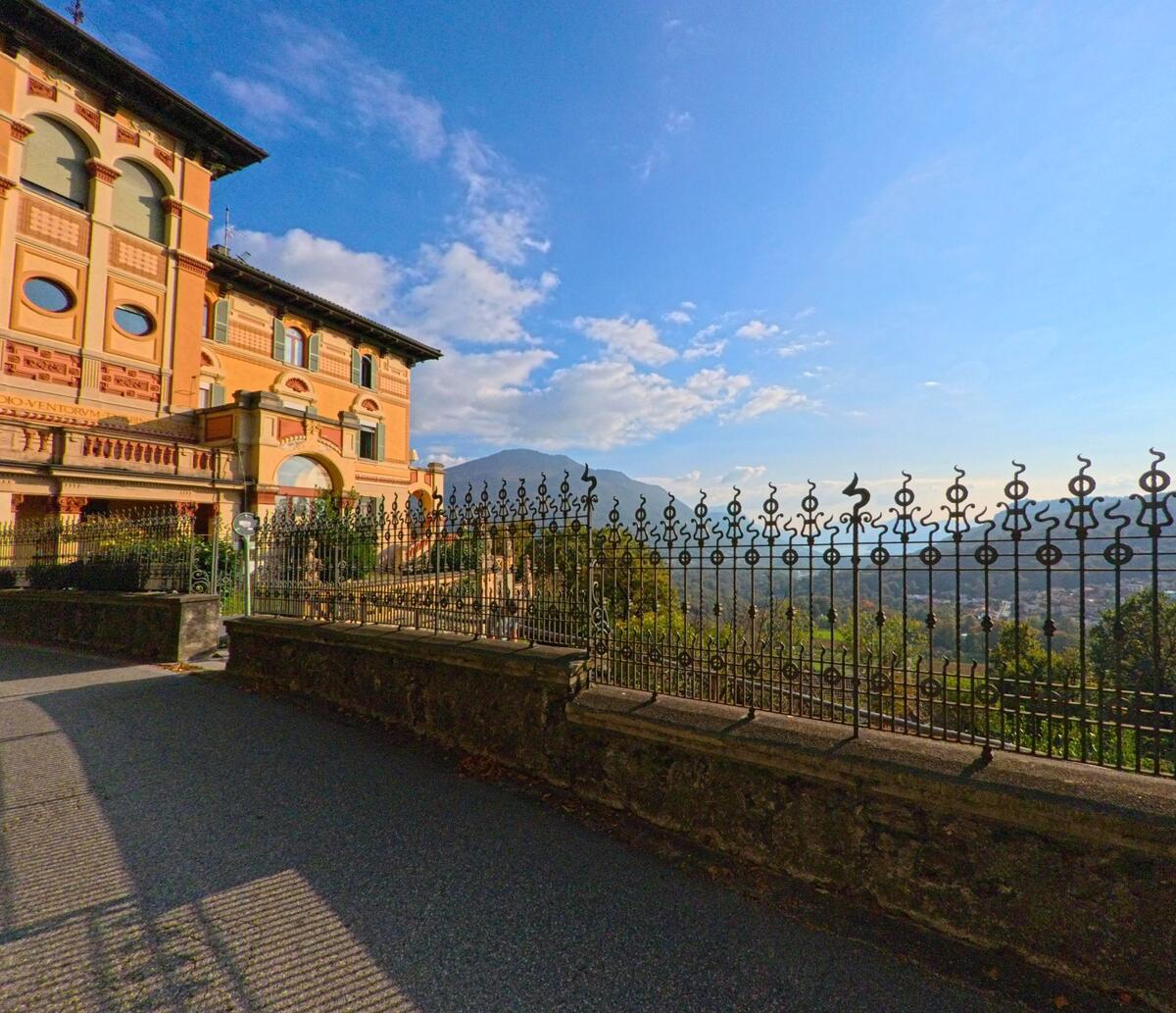 Neben einem reich verzierten historischen Gebäude erstreckt sich ein schmiedeeiserner Zaun mit weiter Aussicht über die Landschaft in Capriasca (6950, Kanton Tessin).