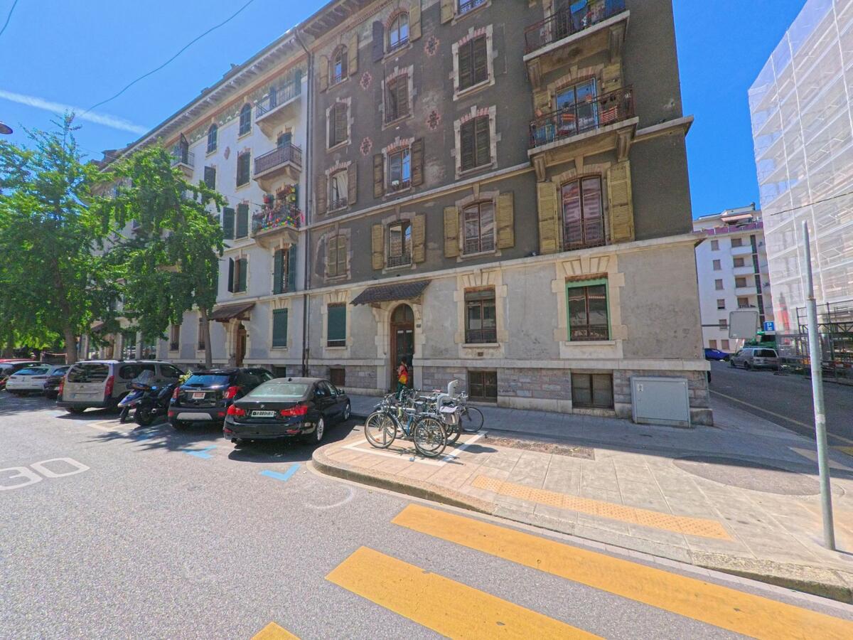Vor einem historischen Wohnhaus mit gruenen Fensterlaeden in Carouge (1227, Kanton Genf) sind Autos und Fahrraeder abgestellt.
