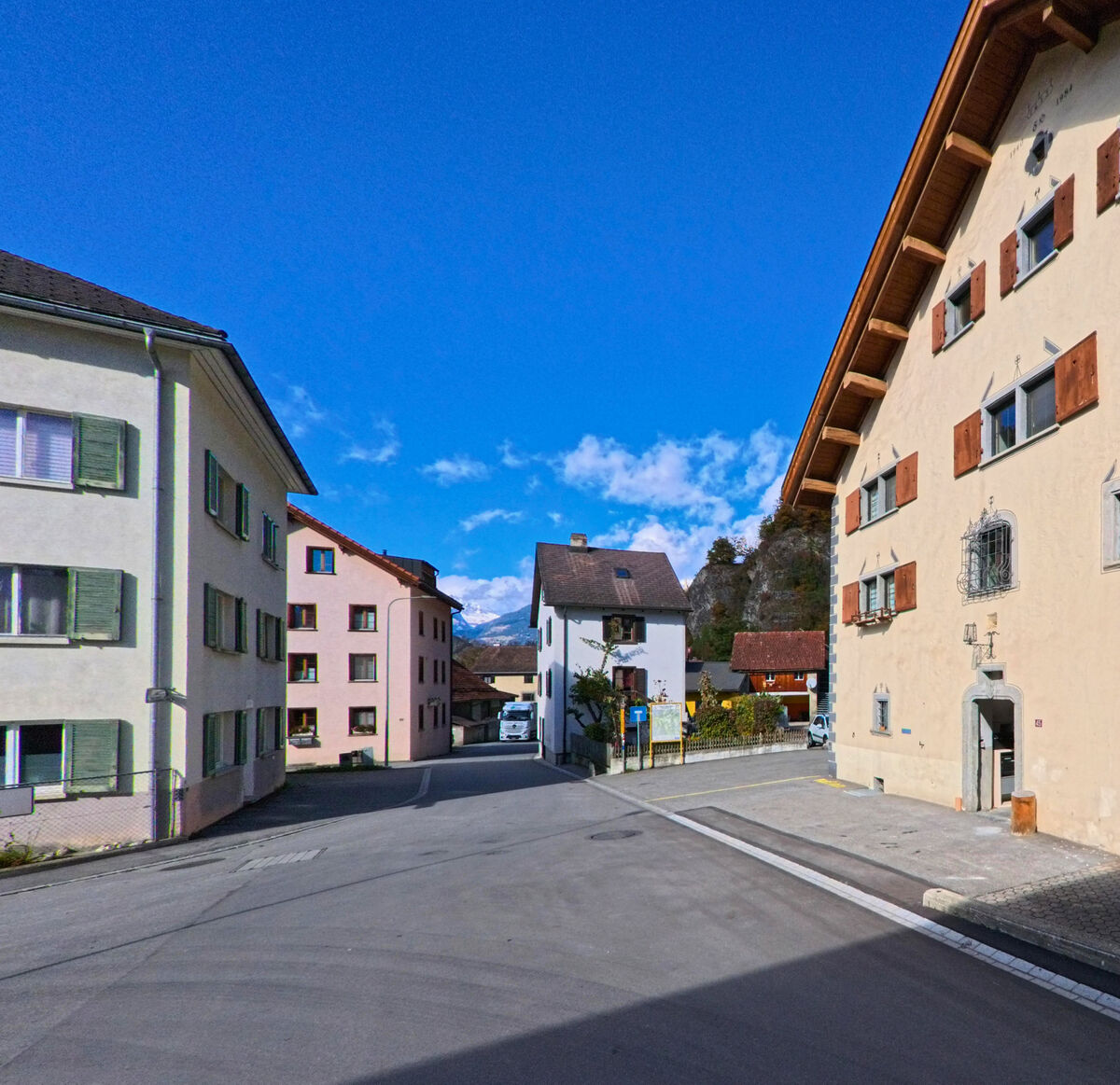 An einer Dorfkreuzung mit Mehrfamilienhaeusern oeffnet sich der Blick in das Siedlungsgebiet von Cazis (7405, Kanton Graubünden).
