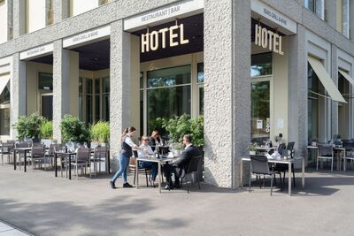 Vor dem Centurion Towerhotel in Windisch (5210, Kanton Aargau) sitzen Gäste an gedeckten Tischen im Aussenbereich, während eine Servicekraft Getränke serviert.