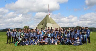 In Wetzikon (8620, Kanton Zuerich) posiert eine grosse Cevi-Gruppe in blauen Hemden vor einem grossen Zelthaus auf einer weitlaeufigen Wiese unter leicht bewoelktem Himmel.