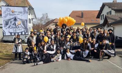 Die Chäslochbrätscher posieren in Deitingen, 4543, Kanton Solothurn, in Fasnachtskostümen mit gelben Ballons und einem Banner für ein Gruppenfoto vor Häusern.