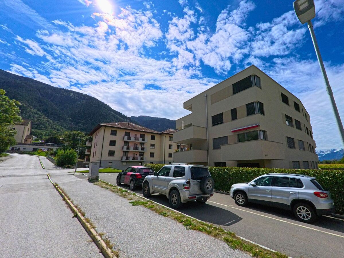 Mehrfamilienhaeuser in Chalais (3966, Kanton Wallis) stehen am Rand einer Strasse, vor den Gebaeuden sind mehrere Autos auf Parkplaetzen abgestellt.